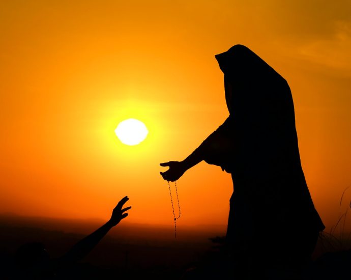 silhouette of woman outstretching hand to help man at sundown